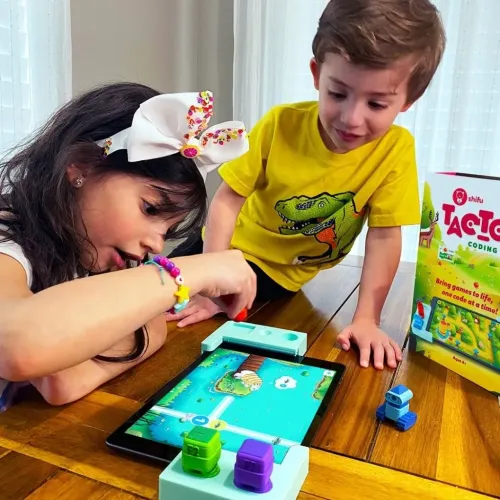 Tacto Coding -pelipakkaus, jossa on kaksi mintunvihreää kehystä tabletin ympärillä ja värillisiä hahmoja, kuvattuna pöydällä pakkauksen vieressä.