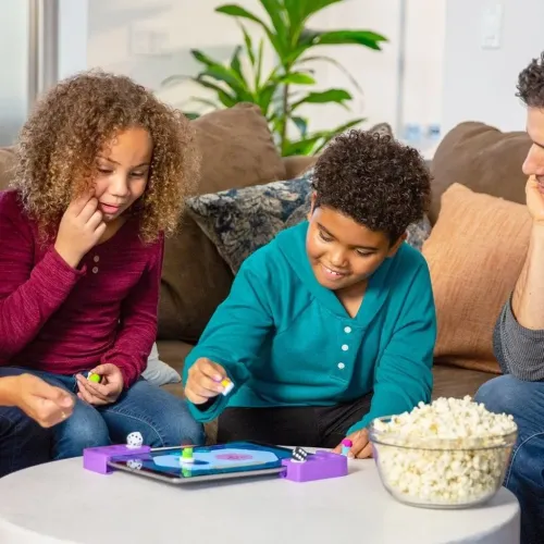 Tacto Classics-rammer på nettbrett med spillebrikker og to terninger på bordet; barn rundt omkring spiller ved salongbordet i stuen.